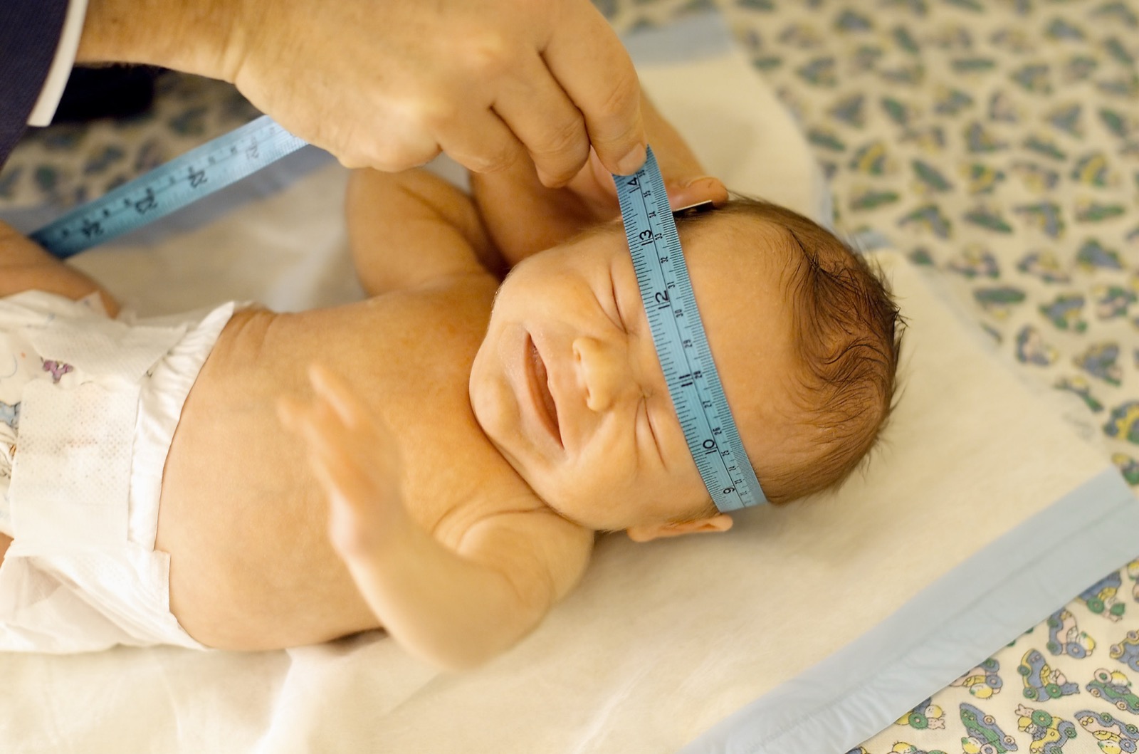 A healthcare provider measures a newborn's head circumference during a wellness check