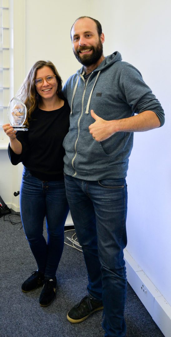 A Dimagi colleague holding a Jen Harlow Award trophy beside a teammate