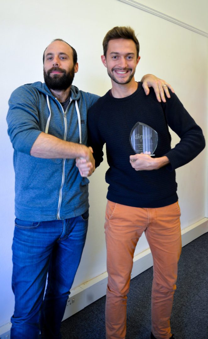 Two Dimagi colleagues shaking hands, one holding a Jen Harlow Award trophy
