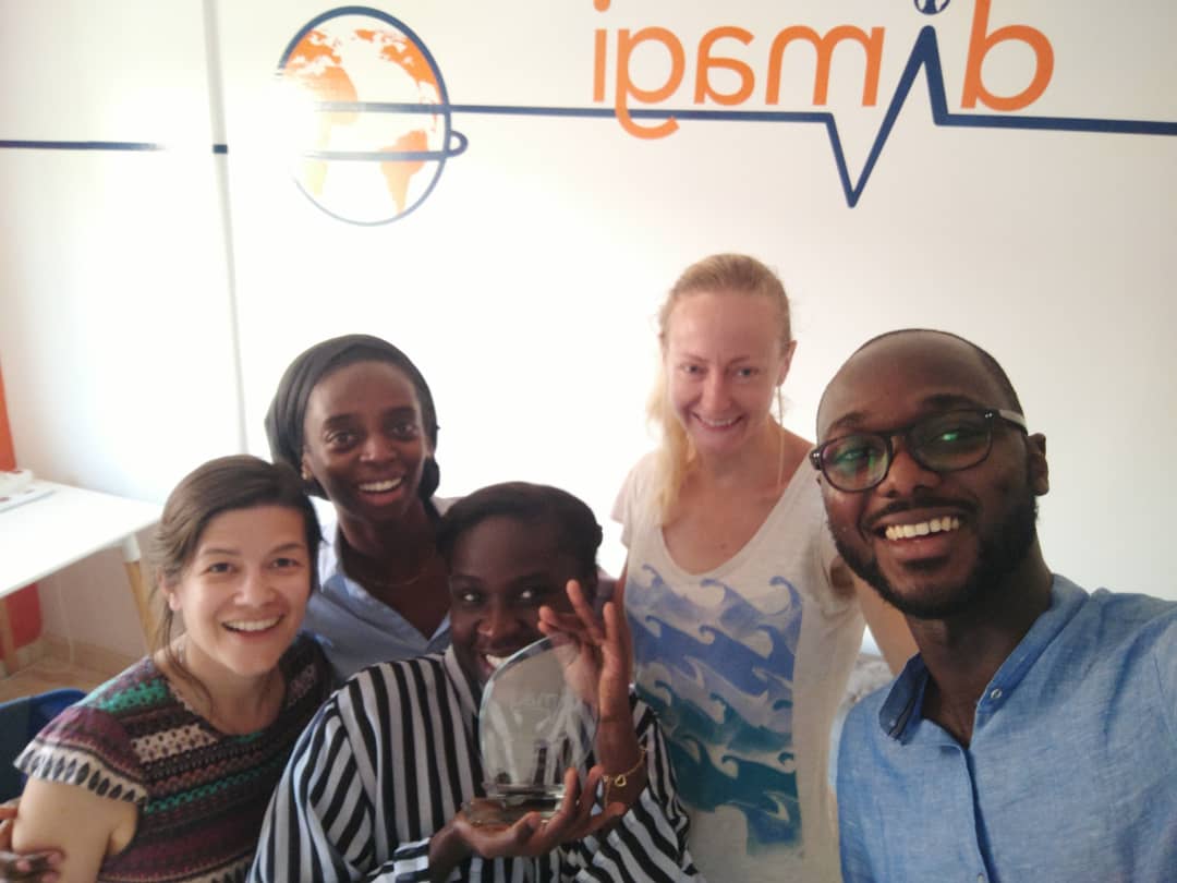 Dimagi team members taking a group selfie in front of the Dimagi logo with a Jen Harlow Award