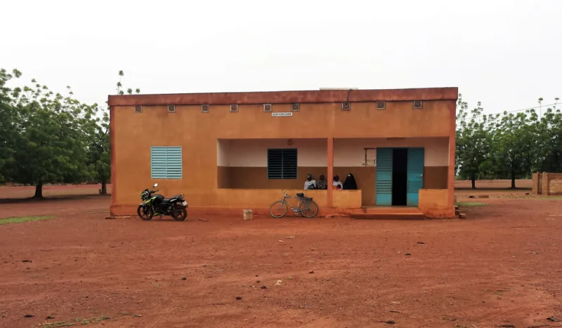 A rural health clinic building with a motorbike and bicycle parked outside