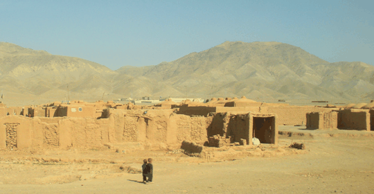 A rural village of mud-brick homes with mountains in the background