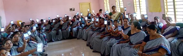 Frontline health workers in saris holding up mobile phones in a training session